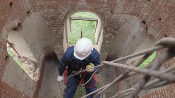 Trabalhador em obras de renovação de edifícios altos em vestuário de protecção. engenheiro de construção avalia o escopo do trabalho. Um alpinista industrial, suspenso por cordas, desce a parede de um edifício. — Vídeo de Stock