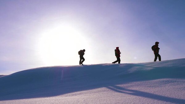 Travelers walk along the top of a snowy ridge in the rays of the beautiful sun. a team of tourists strives for victory and success. business teamwork. beautiful nature of alaska, north.