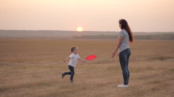 Felice famiglia mamma e bambino giocare frisbee sul campo al tramonto. madre e piccola figlia sana si divertono insieme. mamma e bambino felice stanno lanciando un disco, bambino divertente sta saltando e gioendo. Sport — Video Stock