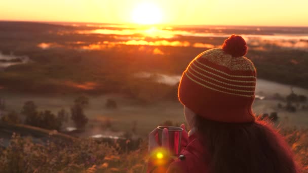 Kobieta Traveler trzyma metalowy kubek z gorącą kawą w rękach i patrzy na wschód słońca z góry. Darmowy turysta dziewczyna podziwiając krajobraz. Turysta pije herbatę z kubka na słońcu. Podróże, kemping — Wideo stockowe