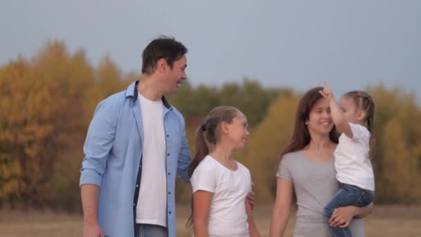 Gelukkige kinderen en ouders wandelen in het park, reizen en ontspannen. gezonde familie speelt in de natuur met dochters. gelukkig glimlachen familie hand in hand, wandelen in het veld, kleine dochter rijden in moeders armen. — Stockvideo