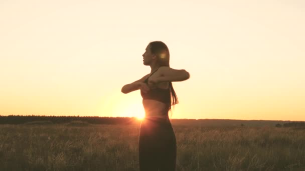 Freie junge Frau treibt Sport im Sommerpark bei Sonnenuntergang. Ein gesundes, schönes Mädchen treibt Sport, außerhalb der Stadt in der Sonne. Workout und Aufwärmen an frischer Luft. Mädchen atmet frische Luft auf dem Feld. — Stockvideo