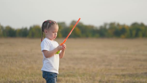 Ein kleines Mädchen bläst bei Sonnenuntergang große Blasen. Die Kindheit eines kleinen Kindes. Kinderspiel im Park — Stockvideo