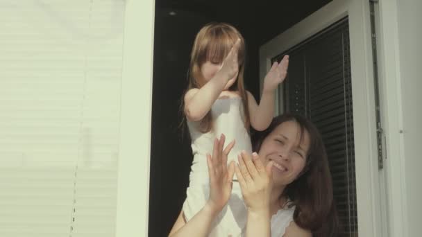 Una famiglia sana respira aria fresca da una finestra aperta. mamma e bambino giocano sul davanzale della finestra in estate. felice madre e figlia guardare fuori dalla finestra battere le mani gioire. — Video Stock