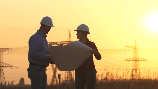 Trabajo en equipo de ingenieros de energía. Un ingeniero y un empresario están estudiando el plan de trabajo. suministro ininterrumpido de electricidad al consumidor. Silueta de ingenieros mira a la construcción de energía de alto voltaje. — Vídeo de stock