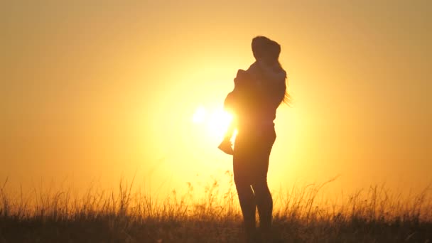 幸せな家族、お母さんは彼女の小さな娘を抱き、彼らは美しい夕日で公園を歩く。子供は太陽の下で母親を抱きしめる。幸せな子供の家族という概念です。母と子は公園を歩いています — ストック動画