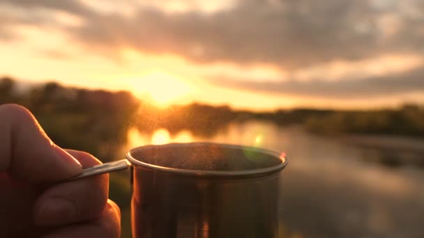 旅行者の手はホットコーヒーと金属マグカップを保持し、日没を見てください。接近中だ。観光客は太陽の下でマグカップからお茶を飲んでいます。アドベンチャー、旅行、観光、キャンプのコンセプト. — ストック動画