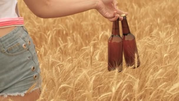 Delicious low alcohol beer drink in hands of a sexy womans hand. a girl with two bottles of beer walks across a wheat field. a farmer brewer carries fresh cold beer through a field of ripe wheat. — Stock Video