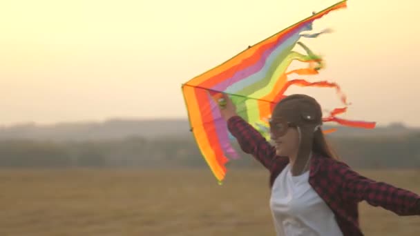 Child dreams of freedom, flight and travel. Happy girl runs in a pilots helmet with a multi-colored kite in her hands in park. teenager wants to become a pilot. teenager playing on a plane outdoors. — Stock Video