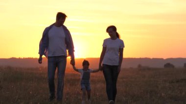 Anne, baba ve çocuk mutlu, kızı gün batımında parkta ebeveynlerinin elini tutuyor. Mutlu aile gün ışığında el ele tutuşarak yürüyor. Sağlıklı bir çocuk ailesiyle oynayıp eğleniyor. Aile.