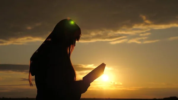 Женщина читает книгу в лучах солнца. Человек читает Библию на улице. Человек держит Библию в своих руках и изучает Слово Божье на восходе солнца на вершине горы. В поисках истины в писаниях. — стоковое фото