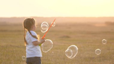 Küçük bir kız gün batımında büyük kabarcıklar çıkarıyor. Küçük bir çocuğun çocukluğu. Parktaki çocuk oyunu