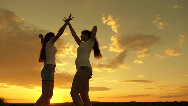 Chicas libres están bailando alegremente en una noche de verano al atardecer. celebración al aire libre. Celebra un día de verano con una fiesta en la playa. adolescentes sanos levantan alegremente las manos. vacaciones divertidas en la orilla —  Fotos de Stock