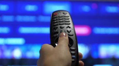 Modern bir uzaktan kumandayla televizyonu kontrol eden bir kişi. Bir adam akıllı bir televizyon izler ve siyah bir uzaktan kumanda kullanır. Bulanık TV kaydırma sayfaları