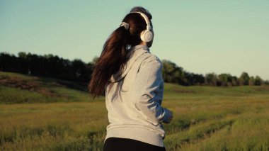 Antrenman koşusu. Özgür genç bir kadın yazın şafak vakti parkta koşar kulaklıkla müzik dinler. Sağlıklı güzel kız spor yapıyor, kırsalda koşuyor. Koşucu kız temiz hava soluyor.