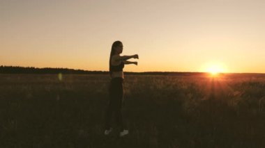 Özgür genç bir kadın gün batımında yaz parkında spor yapmaya gider. Sağlıklı, güzel bir kız şehrin dışında güneşlenir. Egzersiz ve temiz havada ısınma. Kız sahada temiz hava soluyor..