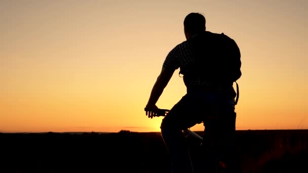 Turista un giovane sano cavalca una bicicletta ai margini della collina, godendo della natura e del sole. Un viaggiatore libero viaggia con una bicicletta al tramonto. concetto di avventura e di viaggio. ciclista solitario che riposa nel parco. — Video Stock