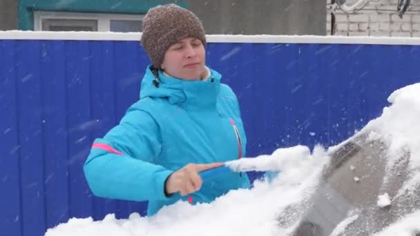 Tyttö pyyhkäisee lunta auton lasista. Nainen puhdistaa auton lumesta harjalla. Kaavin lunta ja jäätä auton tuulilasista. Lumisade peitti auton. — kuvapankkivideo