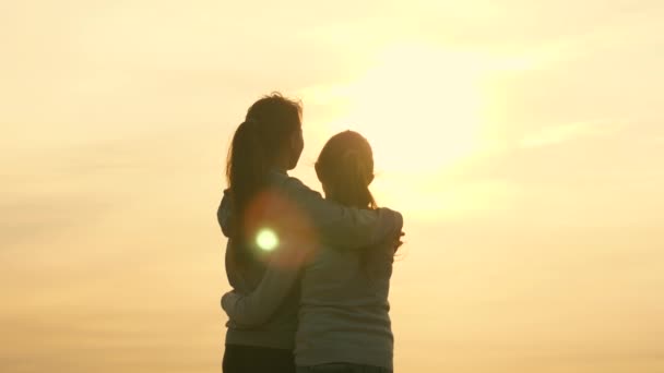 Familia feliz mamá e hija en un campo al atardecer. Concepto de familia feliz de niños y niñas. Mamá abraza a la hija, admiran la hermosa puesta de sol. Madre y bebé caminan en el parque, el campo, en el sol — Vídeo de stock