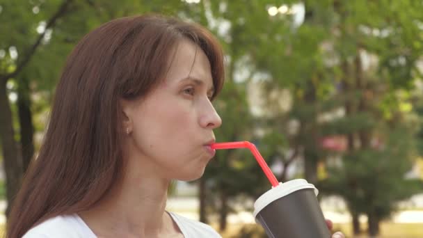 Joven mujer de negocios hermosa está caminando en el parque de la ciudad con una taza de delicioso té para llevar. Mujer feliz bebiendo café aromático caliente al aire libre, riendo, hablando y sonriendo. — Vídeos de Stock