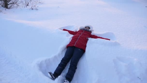Felice bambina sdraiata sulla neve rendendo angelo della neve girato da vista dall'alto il giorno soleggiato alto angolo in movimento lento braccia e gambe sdraiate sulla schiena — Video Stock