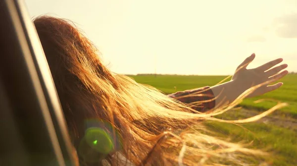 Mujer libre viaja en coche coge el viento con la mano desde la ventana del coche. Chica con el pelo largo está sentado en el asiento delantero del coche, estirando su brazo por la ventana y la captura de resplandor de puesta de sol —  Fotos de Stock