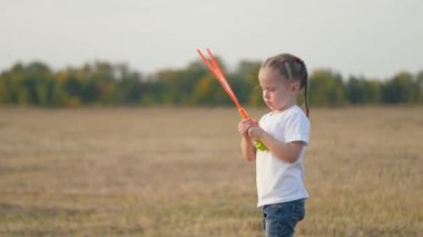 Sağlıklı çocuk parkta sabun köpükleriyle oynuyor. Sahada sabun köpükleri, çocukların doğum günü. Bebek hava kabarcıklarında seviniyor. Kızı gün batımında parkta oynuyor. Mutlu aile ve çocukluk kavramı.