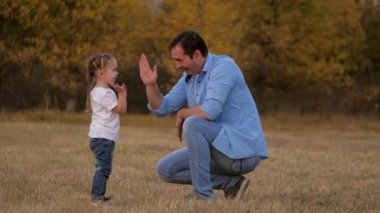 Baba ve küçük kızı merhaba diyor. Çocuk babasını avuç içinde alkışlar, mutlu bir aile parkta oynar. Bebek ve babanın takım çalışması. Eğlenceli bir açık hava oyunu, baba bebeğini seviyor. Sağlıklı aile