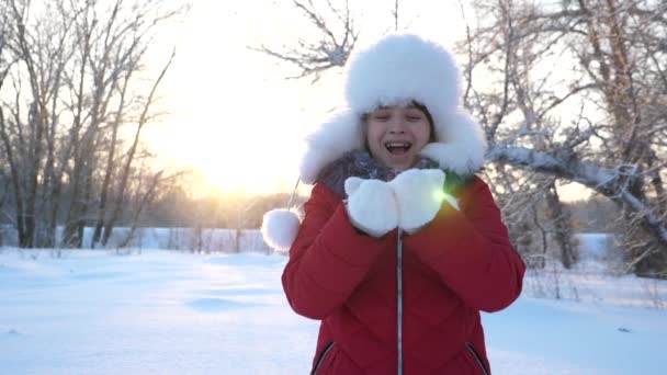 Το χειμώνα, το παιδί παίζει, φυσώντας νιφάδες χιονιού από τις παλάμες του. Κορίτσι φυσάει νιφάδες χιονιού και χαμογελάει στο δάσος. Παίξτε για τις διακοπές Χριστουγέννων σε εξωτερικούς χώρους. Πρωτοχρονιάτικες διακοπές και ευτυχισμένη παιδική ηλικία. Αργή κίνηση. — Αρχείο Βίντεο