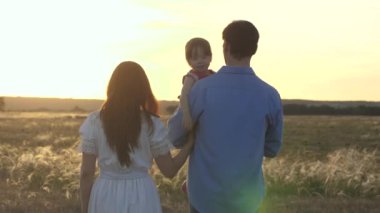 Kollarında çocuk olan mutlu bir aile güneşte tarlada yürüyor. Sağlıklı küçük kız yaz parkında anne ve babasıyla oynuyor. Ebeveynler çocuklarıyla seyahat ederler. Sağlıklı aile kavramı, çocukluk.