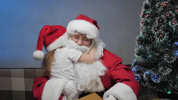 Küçük kız Noel Baba 'ya sarılıp öpüyor. Çocuk sihirli büyükbaba Noel Baba ile tanıştığı için mutlu. Çocuk için iyi tatiller. Kış masalı ziyaretçi çocuğu. Kış tatili yeni yıl. Nazik büyü dede. — Stok fotoğraf