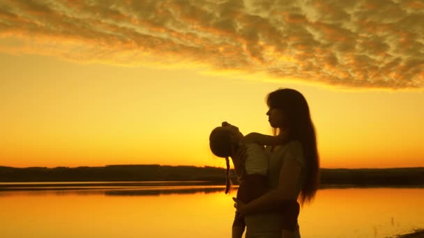 Famiglia felice, mamma che si abbraccia al tramonto con la figlioletta felice sulla spiaggia. Mamma gioca con il suo bambino in acqua al tramonto. Felice concetto di famiglia. Silhouette di madre e bambino sano che balla. — Video Stock