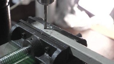 Sondaj makinesi metal bir parçayla bir delik açar. Çilingir atölyesindeki bir fabrikada tamirci. Sondaj makinesi. Bir makine işçisi demir bir işyerinde delik açıyor..