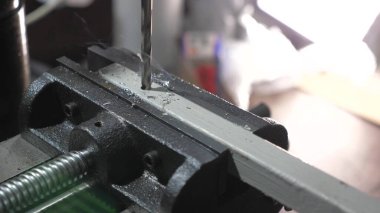 Sondaj makinesi metal bir parçayla bir delik açar. Çilingir atölyesindeki bir fabrikada tamirci. Sondaj makinesi. Bir makine işçisi demir bir işyerinde delik açıyor..
