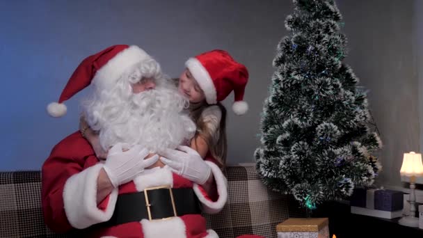 Święty Mikołaj siedzi na kanapie, dziewczyna, dziecko bawi się z nim, raduje się i przytula magicznego dziadka. Koncepcja świąt i uroczystości. Rodzinne dzieci zimowe wakacje. Wesołych Świąt. — Wideo stockowe