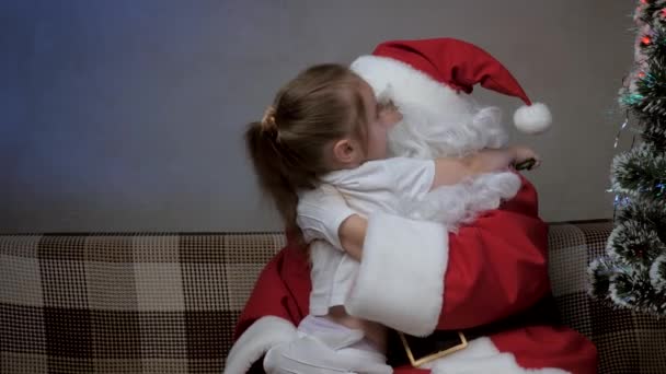 Dziecko jest szczęśliwy, aby poznać magicznego dziadka Świętego Mikołaja. Wesołych świąt dla dziecka. Dziewczynka przytula i całuje Świętego Mikołaja. Zimowa bajka odwiedzająca dziecko. Wakacje zimowe nowy rok. Miły magiczny dziadek — Wideo stockowe