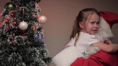 Küçük kız ağlıyor ve Noel Baba 'ya sarılıyor. Çocuk üzgün, Noel Baba onu sakinleştiriyor. Mutlu çocuk tatilleri. Çocuğu ziyaret eden bir kış masalı. Kış tatili yeni yıl. Nazik büyü dede.