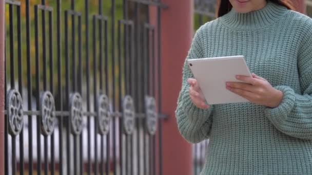 Dziewczyna używająca tabletu cyfrowego drukuje wiadomości na ulicy. Studentki dotykają tabletów dotykiem. Kobieta pracuje z tabletem, spacerując po chodniku w mieście. — Wideo stockowe