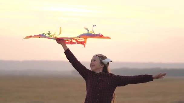 Child dreams of freedom, flight and happy family. Teenager plays by airplane outdoors. Happy girl runs with a multi-colored kite in her hands to field in rays of sun. Teenager wants to become a pilot. — Stock Video
