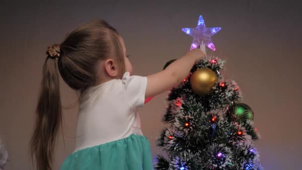 Child hangs golden toy ball on Christmas tree. Beautiful little girl decorates Christmas tree with colorful balls. Happy family, childhood, Christmas. Kid playing on christmas eve. Holiday celebration — Stock Video