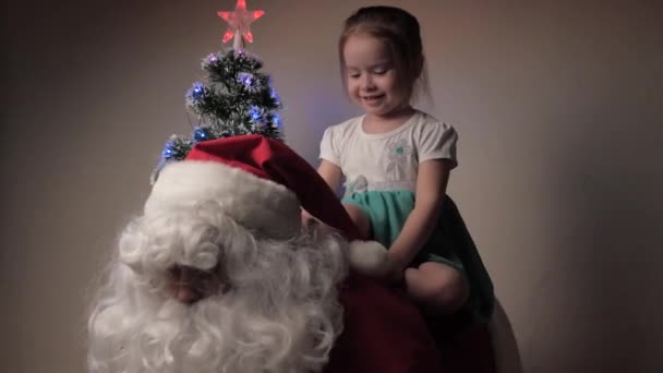 Child and Santa Claus are playing together, a little girl is sitting on back of Santa Claus. Santa Claus having fun with kid next to Christmas tree. Family holiday, winter vacation. Merry Christmas. — Stock Video