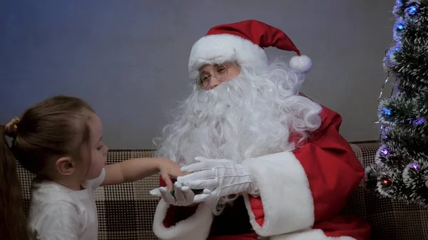 Santa Claus sits on couch with a little girl, Santa gave a gift to toy car, child rejoices and hugs magic grandfather. holiday and celebration. Family childrens winter vacation. Happy Christmas Eve. — Stock Photo, Image