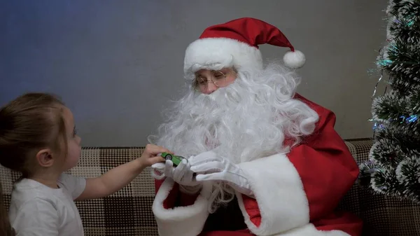 Jultomten sitter på soffan med en liten flicka, jultomten gav en gåva till leksaksbilen, barn jublar och kramar magiska farfar. semester och fest. Familjens barn vintersemester. Grattis på julafton. — Stockfoto
