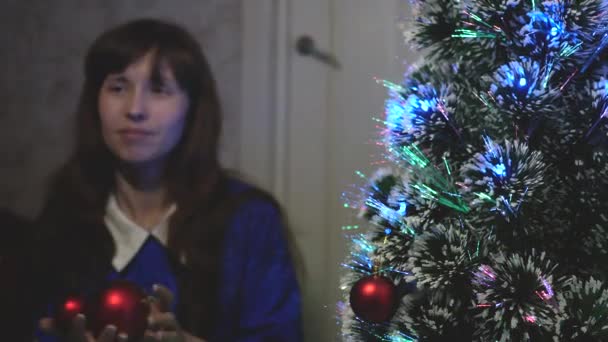 小さな娘と母親はクリスマスツリーに赤いおもちゃのボールをぶら下げています。幸せな家族クリスマス。赤ちゃんとお母さんはクリスマスボールでクリスマスツリーを飾る。陽気な子供とママが木で遊んでいる. — ストック動画