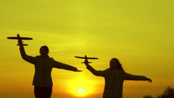 Silhuett av barn som leker på plan. Drömmar om att flyga. Glad barndomsidé. Två flickor leker med ett leksaksplan vid solnedgången. Barn på bakgrunden av solen med ett flygplan i handen. — Stockvideo