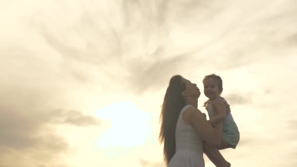 Šťastná matka a malé zdravé dítě se objímají v parku na přírodě v paprscích slunce. Máma vyhodí svou milovanou zdravou dceru do nebe v náručí. Rodina na dovolené. Máma a dítě při západu slunce. — Stock video