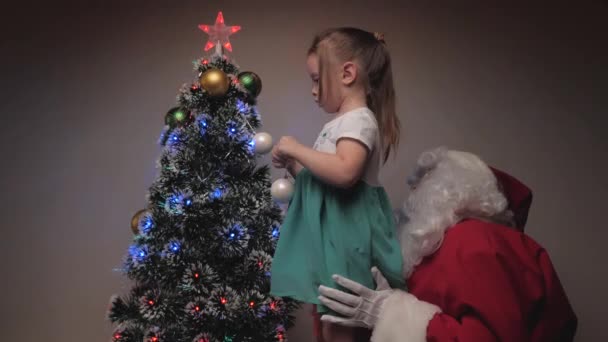 Child and Santa Claus decorate the Christmas tree. A little girl and Santa Claus hang beautiful balls on the tree. Holidays and celebrations. Family childrens winter vacation. Merry Christmas. — Stock Video