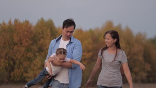 Glad leende familj som håller hand, går i fält, liten dotter som flyger i pappas armar. Barn och föräldrar går i parken, reser och kopplar av. En frisk familj leker utomhus — Stockvideo