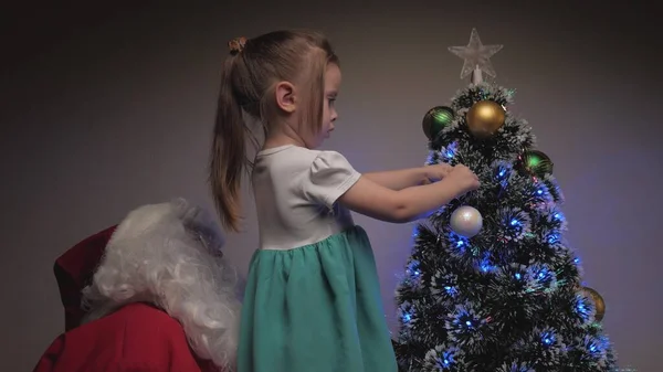 Una bambina e Babbo Natale appendono belle palle sull'albero. Buon Natale. Ciao. Bambino e Babbo Natale decorano l'albero di Natale. Feste e celebrazioni. Vacanza invernale per bambini in famiglia. — Foto Stock