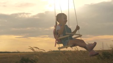 Sağlıklı mutlu çocuk parkta salıncakta uçar. Küçük neşeli bir kız güler, sevinir ve uçarken kollarını sallar. Annem kızını güneşin altında salıncakta sallıyor. Aile ve çocukluk